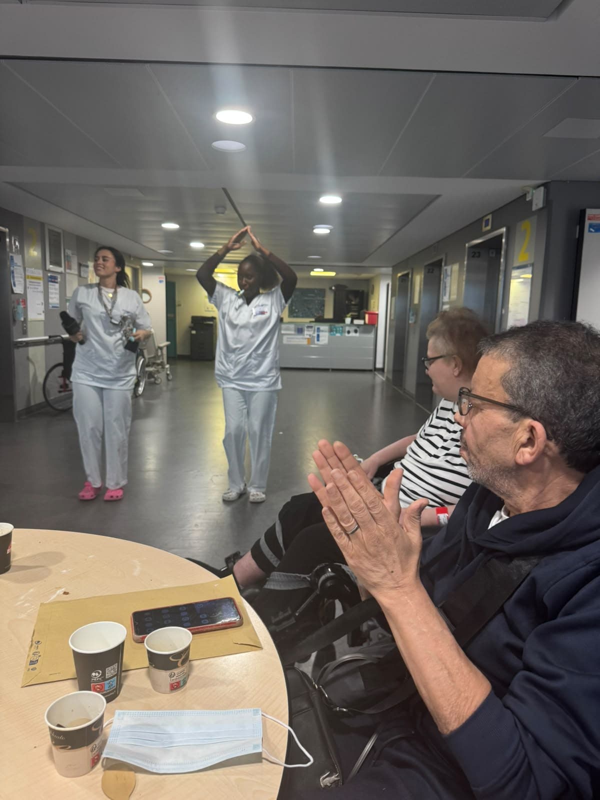Deux bénévoles dansent les bras levés devant des patients qui applaudissent.